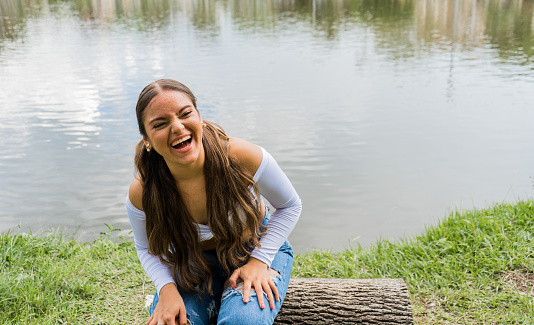 very happy and smiling long-haired young woman sitting by a lake