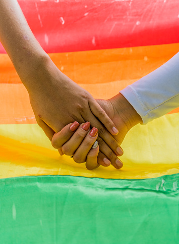 female hands held in a background of the LGBTIQ+ flag