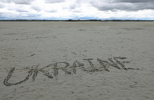 very big UKRAINE text etched into the beach sand at low tide