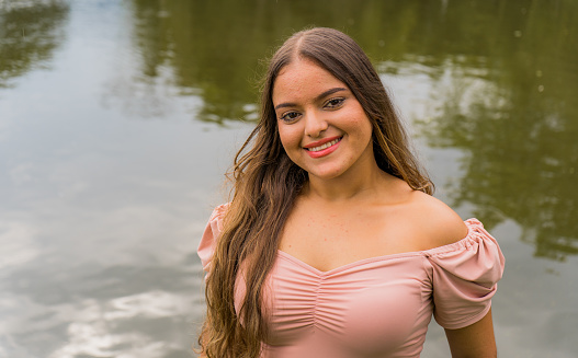 young woman smiling and in the background a lake reflecting the clouds