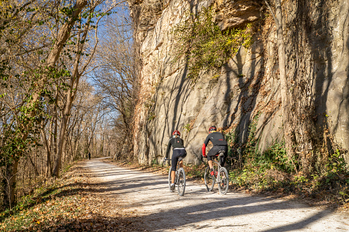 Rocheport, MO, USA - November 18, 2023. A couple of cyclists on Katy Trail in late November scenery with a rocky cliff.