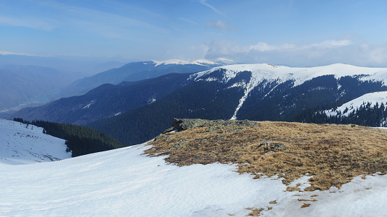 A valley seen from top of a mountain in late winter season. The coniferous forests and the mountain peaks are still covered with snow. Carpathia, Romania.