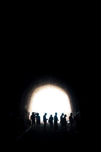 A group of tourists seen in profile from a distance. This perfectly backlit photo was taken in a tunnel where the only source of light is the exit at the far end.