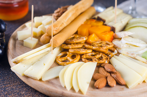 Delicious cheese mix with grapes, jam, snacks, crackers, walnuts and vine on a wooden board. Dinner or aperitif concept. Exquisite cheese plate, wine food.