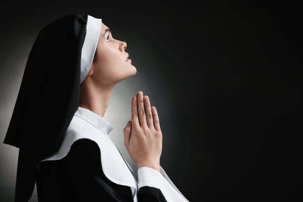 istock Nun with clasped hands praying to God on black background. Space for text 1823060486