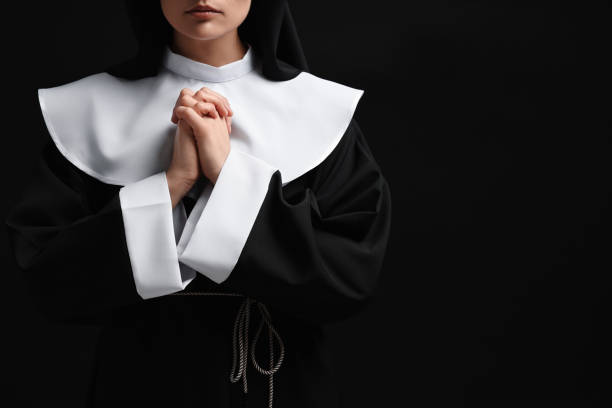 istock Nun with clasped hands praying to God on black background, closeup. Space for text 1823061034