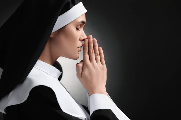 istock Nun with clasped hands praying to God on black background. Space for text 1823061542