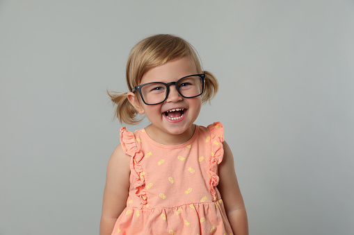 Cute little girl in glasses on light grey background
