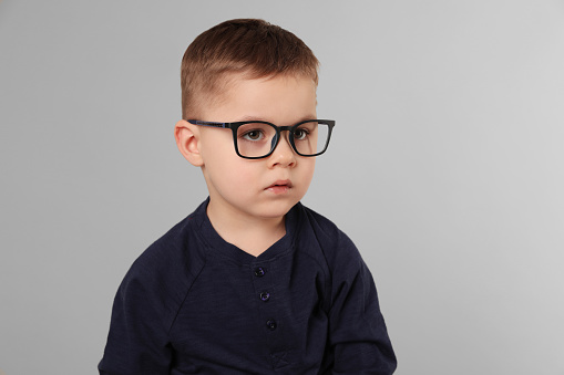 Cute little boy in glasses on light grey background