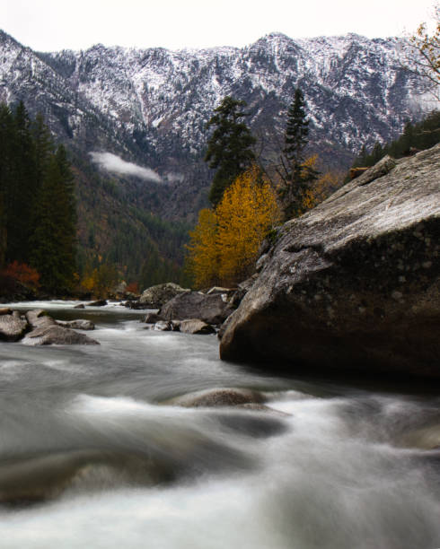 otturatore ritardato con rapide d'acqua bianca lisce attraverso il fiume coperto di roccia a washington con la catena montuosa delle cascate del nord sullo sfondo con fogliame autunnale - north cascades national park cascade range river waterfall foto e immagini stock