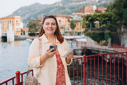 Hipster girl with two tickets browsing Internet. Cruise ship vacation concept. Varenna, Italy. Lake Como. Female holding phone and booking hotel