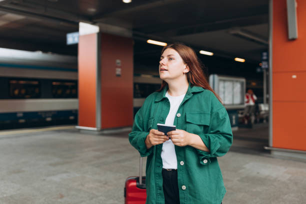 istock Young redhead woman waiting train with backpack and using smart phone. Railroad transport concept, Traveler. 30s Woman with suitcase walking at railroad station platform. Travel to vacation by train 1823135145