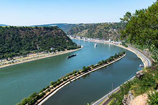 View from the Loreley viewpoint at the river Rhine with a cargo ship and a recreational vessel. The town of Sankt Goarshausen is seen in the background. The viewpoint on top of the Loreley rock is at an altitude of 125 meters over the Rhine.