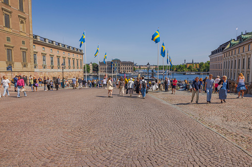 Sweden. Stockholm. 06.06.2023 View of people on cobblestone street descending towards waterfront in central Stockholm, by royal castle. Square is adorned with flags, celebrating Sweden's National Day.