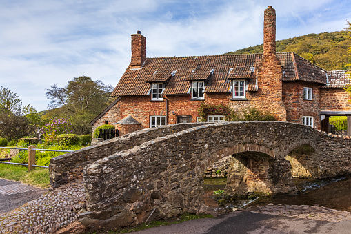 The medieval packhorse bridge and pretty cottages in the picturesque Allerford village on Exmoor National Park in Somerset.