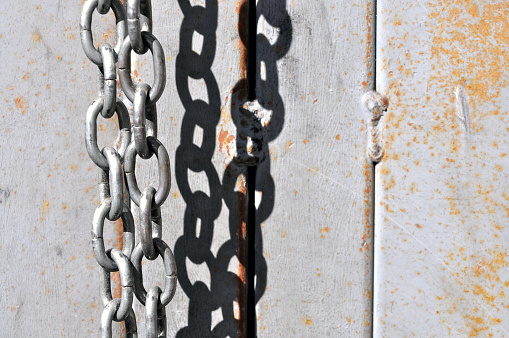 Rusting metal chains hanging in bright sunlight create a quiet still-life and series of shadows in the background.