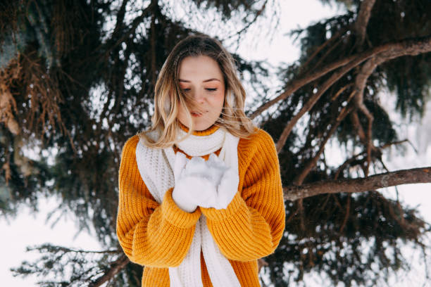 Teen blonde in a yellow sweater outside in winter. A teenage girl on a walk in winter clothes in a snowy forest stock photo