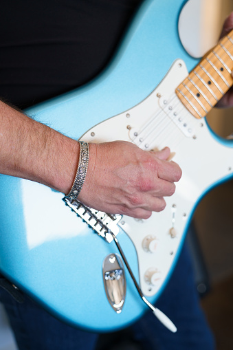Close-up, cropped in shot of a musician's hands playing a blue and white electric guitar and wearing a silver cuff bracelet