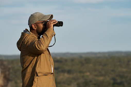Young man looking through binoculars on a hill in a nature reserve