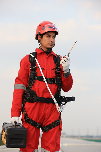 Portrait of Solar engineer wearing red safety uniform,  red hardhat, and hardness safety belt holding toolbox and walkie talkie  working on solar rooftop