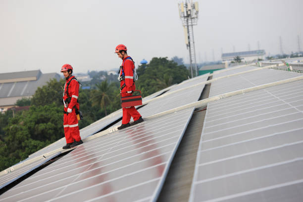 Maintenance power  engineer team wearing red safety uniform and safety hardness hold toolbox walk on the solar rooftop, Green Renewable energy for industry concept