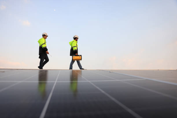 istock Two special Electrical engineers in safety suits worked and checked the solar system on the roof after installing,  walking on the roof against the blue sky and photovoltaic panel. 1823326747