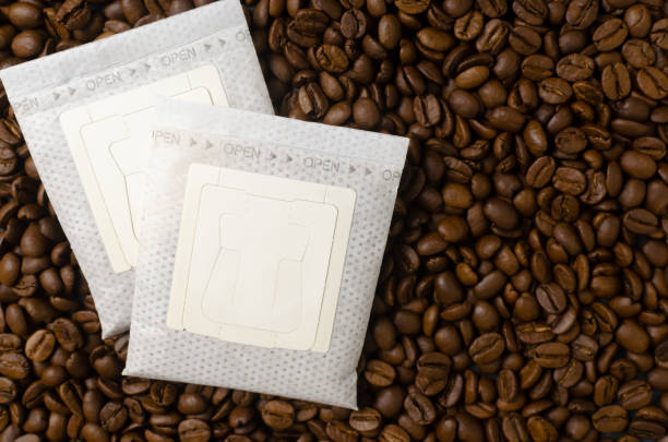 Two drip coffee bags on a background of beans. A quick way to prepare a tasty and aromatic drink. Horizontal orientation. Top view. Copy space stock photo