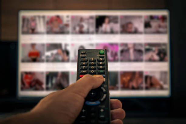 pornografia na tv. controle remoto na mão de um homem no fundo de um filme erótico em fora de foco. conteúdo adulto no canal a cabo do hotel - internet computer monitor discussion surfing the net - fotografias e filmes do acervo