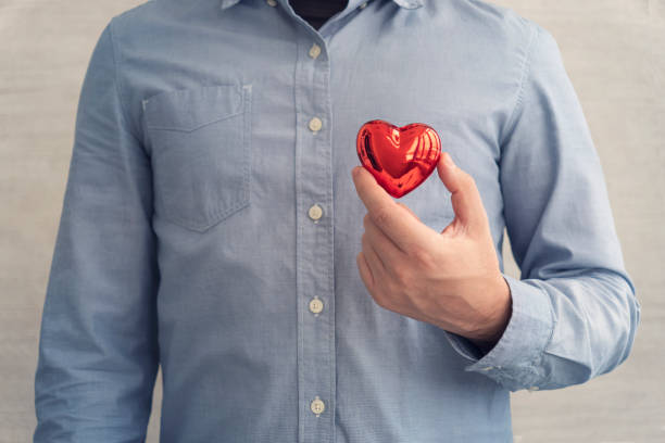 파란 셔츠를 입은 남자는 사랑과 건강의 상징인 빨간 하트를 손에 들고 있습니다 - heart shape business valentines day businessman 뉴스 사진 이미지