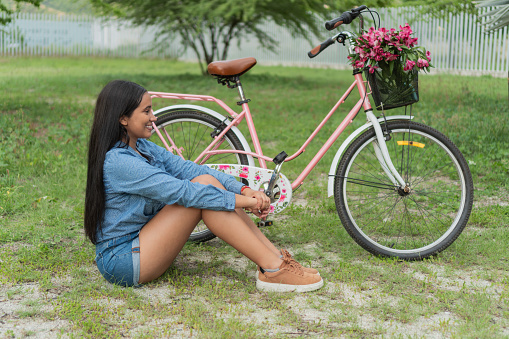 Woman sitting next to her classic bicycle on a sunny afternoon in rural Latin America.