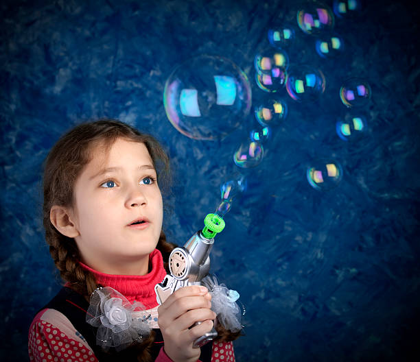 Young girl making blow bubbles with soap gun. Studio shot with vignetting effect