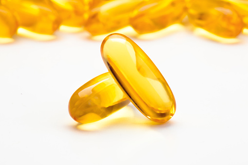 Fish oil softgel capsules scattered on a white table, focus on foreground.