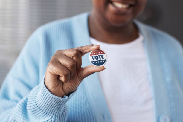 Focus on hand of young African American woman holding small badge Focus on hand of young African American woman in casualwear holding small round vote badge while standing in front of camera civilized stock pictures, royalty-free photos & images