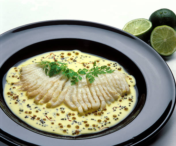 Close up on a black gourmet dish with poached ray wing with parsley in safran sauce, lime on the side.