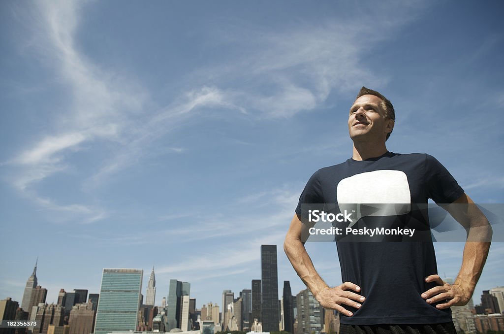 Man in Blank Quote T-Shirt Standing in front of Skyline Man wearing a t-shirt with a blank quote bubble standing with hands on hips against blue sky in front of city skyline Adult Stock Photo