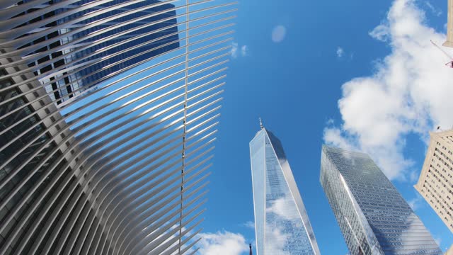 Timelapse, amazing view of the the Freedom Tower, One World Trade Center and Oculus in Lower Manhattan, New York against the cloudy blue sky reflecting on the glass skyscraper