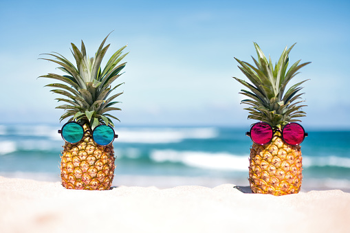 Two pineapples with trendy sunglasses on the beach
