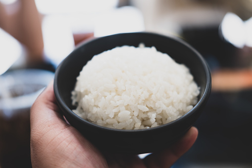 Hands holding a black bowl of rice.