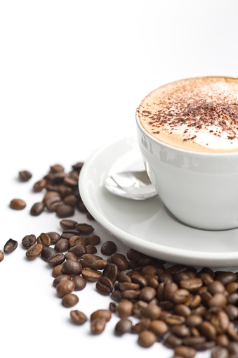 Cropped coffee cup of Cappuccino with froth and chocolate powder, with a scattering of roasted coffee beans on a white background.