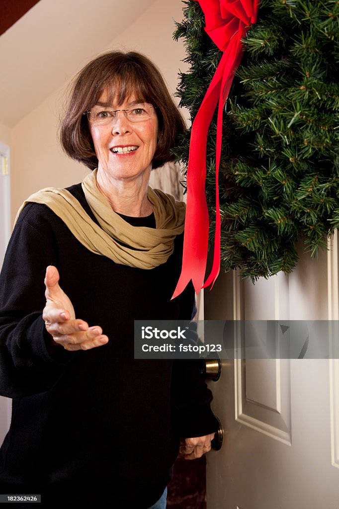 Senior woman opening front door Christmas wreath Senior Adult Stock Photo