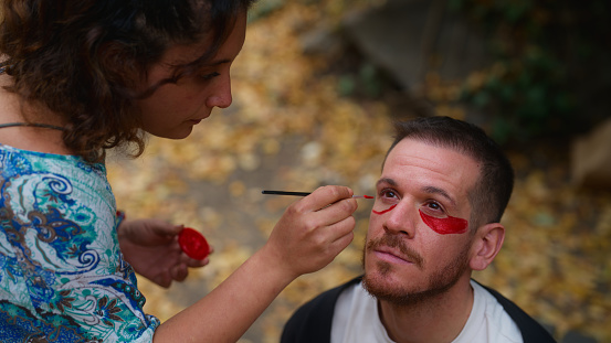 Friends are painting their faces for an outdoor spiritual ecstatic dance party event in nature.