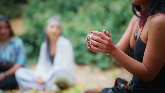 A woman in a black dress is serving cacao drinks during a cacao ceremony in nature. 
A cacao ceremony is a spiritual ritual for cleaning soul, connecting with the nature, healing, mental wellbeing, mindfulness and self-exploration. People who join the ceremony consume ceremonial cacao.