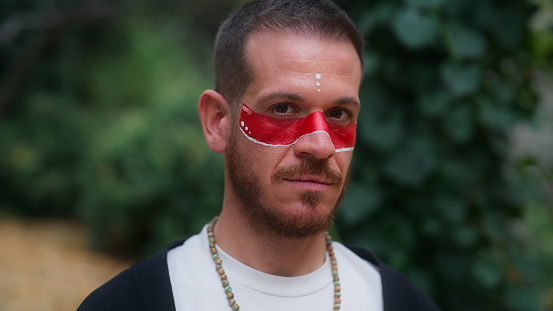 A portrait of a spiritual man with red colored face paint in nature.
