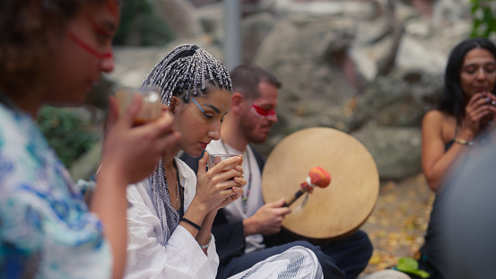 A group of multi-ethnic friends are gathering in nature and having cacao tea drink ceremony.\nA cacao ceremony is a spiritual ritual for cleaning soul, connecting with the nature, healing, mental wellbeing, mindfulness and self-exploration. People who join the ceremony consume ceremonial cacao.