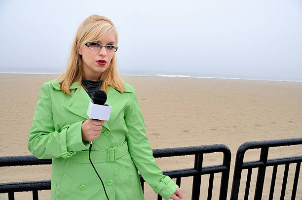 News Reporter Comments on Empty Beach "Young blonde female reporter/weather girl on location during inclement weather. Series shot at Hampton Beach, NH." mike cherim stock pictures, royalty-free photos & images