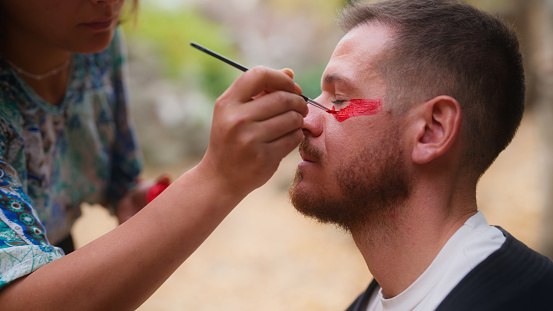 Friends are painting their faces for an outdoor spiritual ecstatic dance party event in nature.