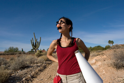 Young adult female outside on dirt road wearing silly glasses and holding megaphone.