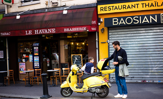 Paris, France: A father, his child, and a yellow scooter outside a sidewalk cafe in the 9th arrondissement.