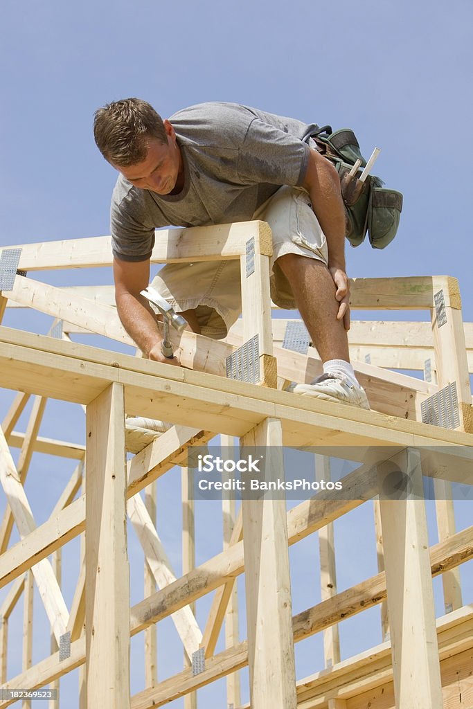 Builder Hammering tetto capriate chiodo contro il cielo blu - Foto stock royalty-free di Attrezzi da lavoro