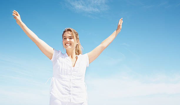 istock Happy young lady with arms raised against blue sky 182369866